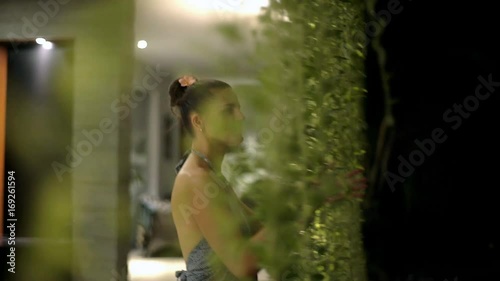 Attractive woman walking through hanging plants to the garden at night, steadycam shot
