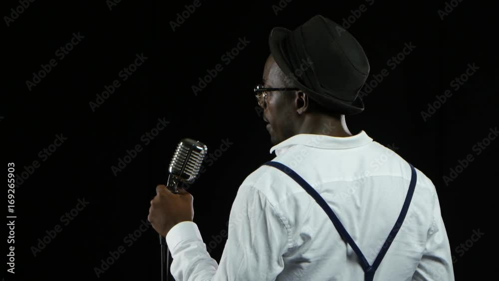 Man african american the view from the back standing at the microphone professionally singing in a recording studio. Black background. Close up Man african american the view from the back standing at the microphone professionally singing in a recording studio. Black background. Close up