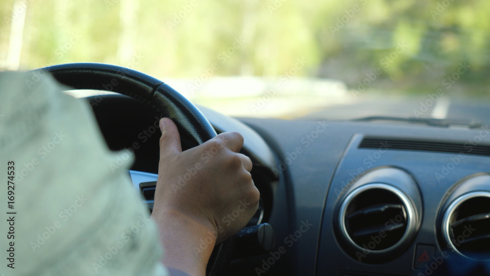man's hand on the steering wheel driving a car in the long road along mountains