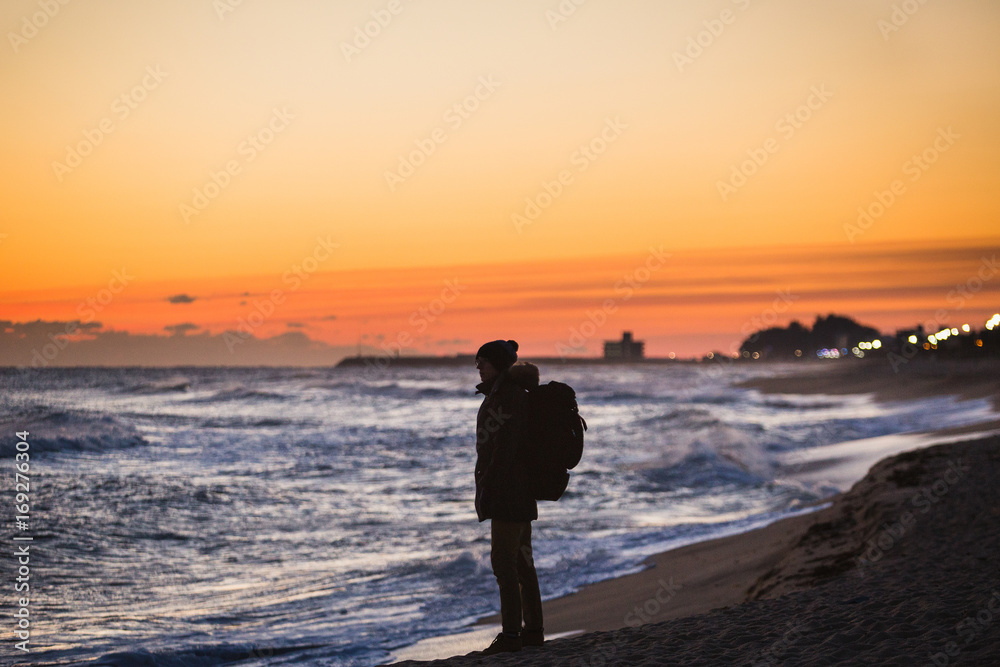 A traveler with a backpack is standing on the shore of Japanese Sea and looks at the sunrise.