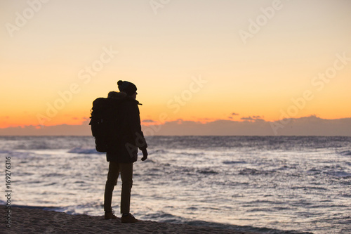 A traveler with a backpack is standing on the shore of Japanese Sea and looks at the sunrise.