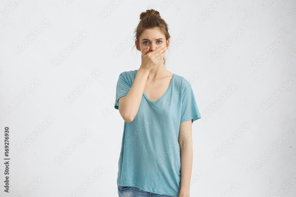 Beautiful woman with blue charming eyes, dressed casually, covering mouth with hands while trying to be silent and not to tell big secret. Attractive female stopping gossiping, keeping hand on mouth Beautiful woman with blue charming eyes, dressed casually, covering mouth with hands while trying to be silent and not to tell big secret. Attractive female stopping gossiping, keeping hand on mouth