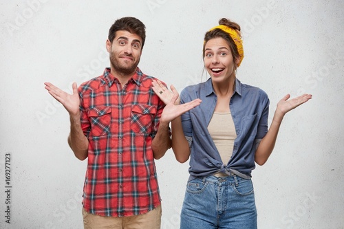 Things happen. Picture of funny friendly-looking European male and female in love dressed causally having confused and clueless expressions, shrugging shoulders, meaning: So what? Who cares? photo