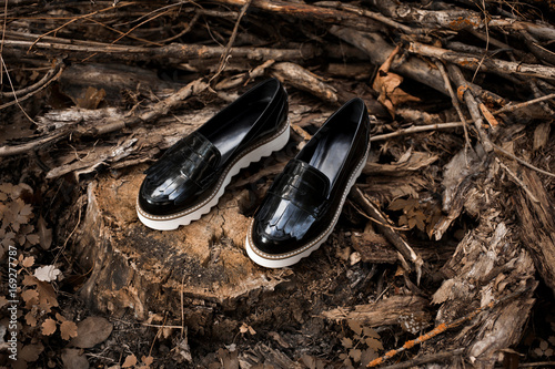 Bilde på lerret Black shiny patent leather womens loafers with white soles on old wood in a forest or park