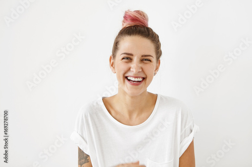 Beautiful playful young European female wearing white oversize t-shirt with rolled up sleeves laughing at good joke, her look and expression full of joy and happiness. People and lifestyleconcept photo