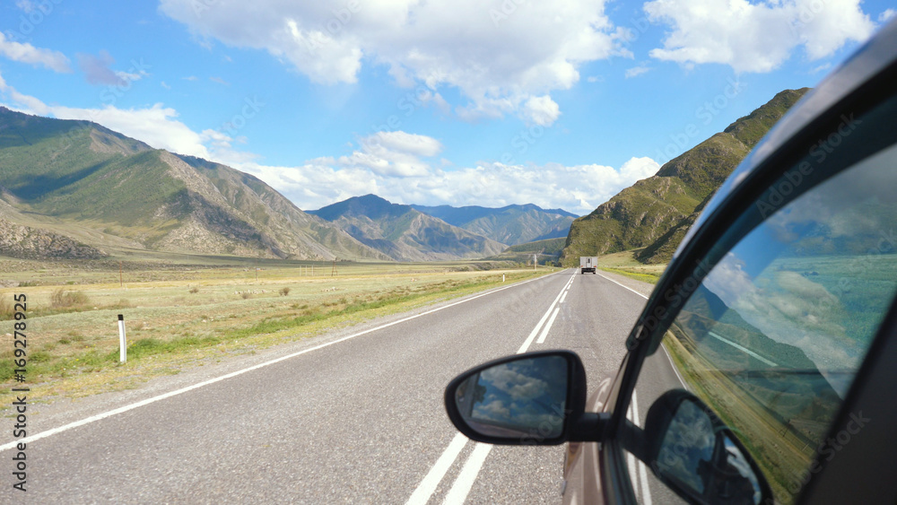 Driving view from side of car mirror mountain valley. Beautiful landscape of a road in the mountains on sunny day