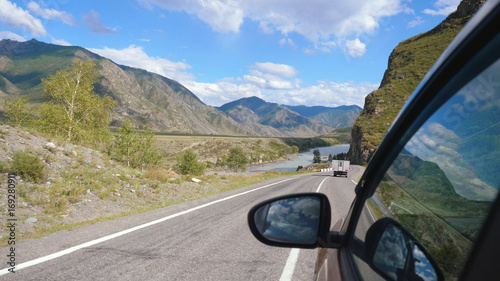 Driving view from side of car mirror mountain valley. Beautiful landscape of a road in the mountains on a sunny day