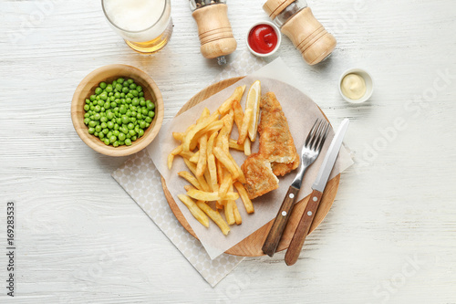 Fried fish and chips with peas on white wooden background