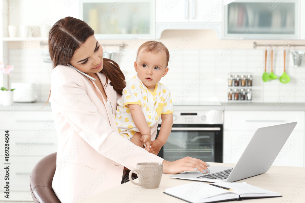 Young mother holding baby while working in home office Young mother holding baby while working in home office