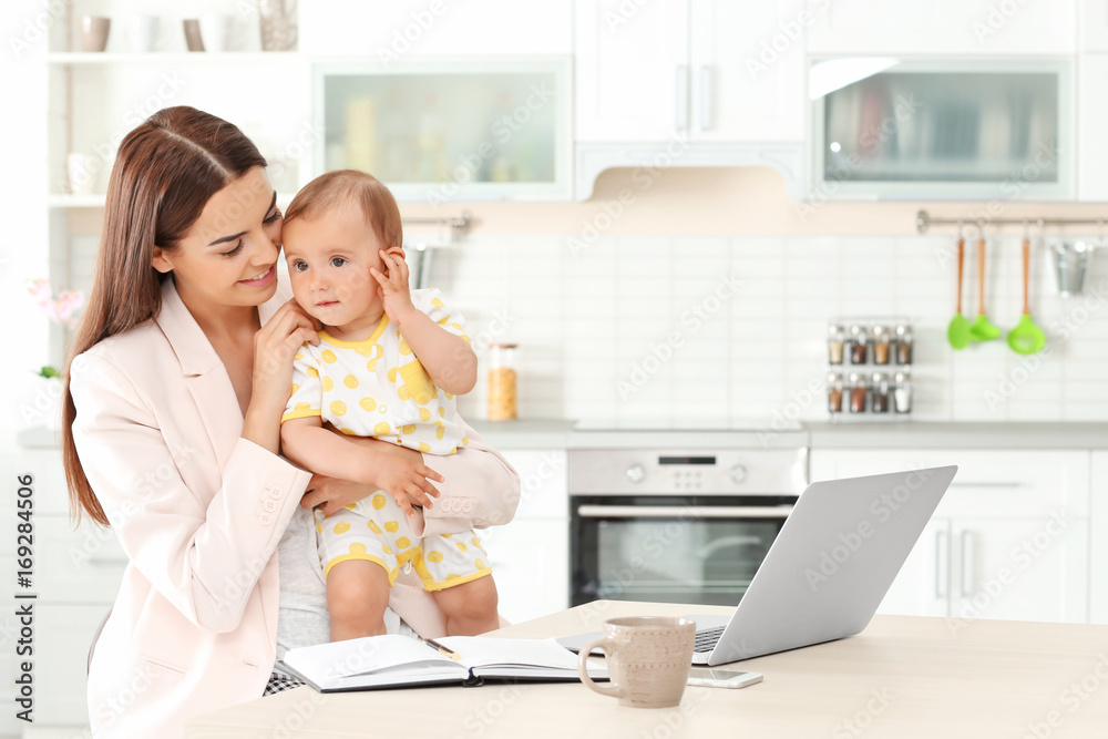 Young mother holding baby while working in home office