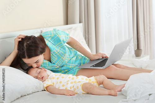 Young mother kissing sleeping baby on bed