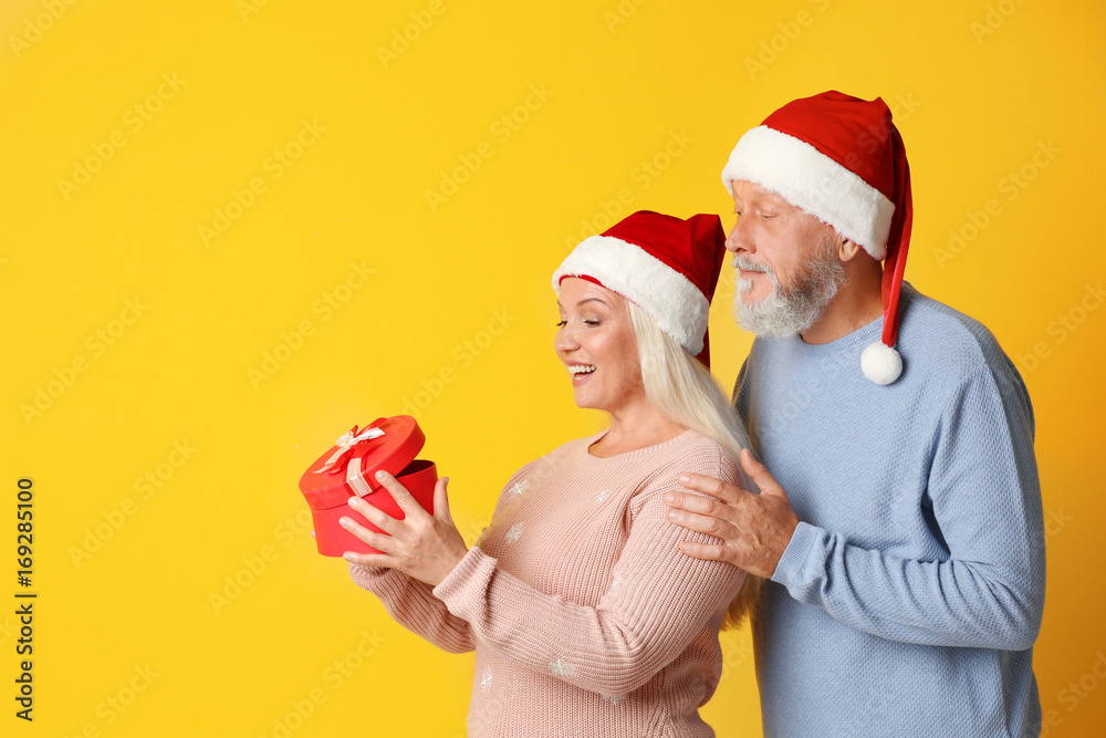 Obraz premium Happy senior couple with Christmas gift on color background