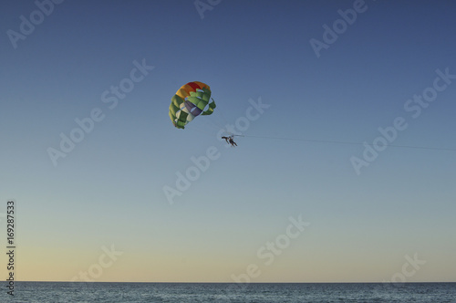 Люди летят на парашюте над морем на закате