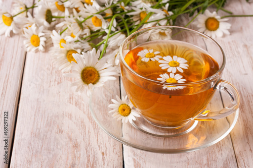 Herbal tea with fresh chamomile flowers on white wooden background