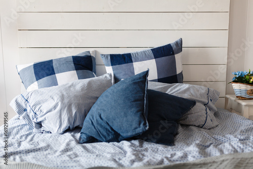 Sloppily made bed with a blue pillow with a checkerboard pattern. photo