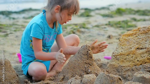 Close-up a six-year girl builds a sand castle on the beach on the sea coast.