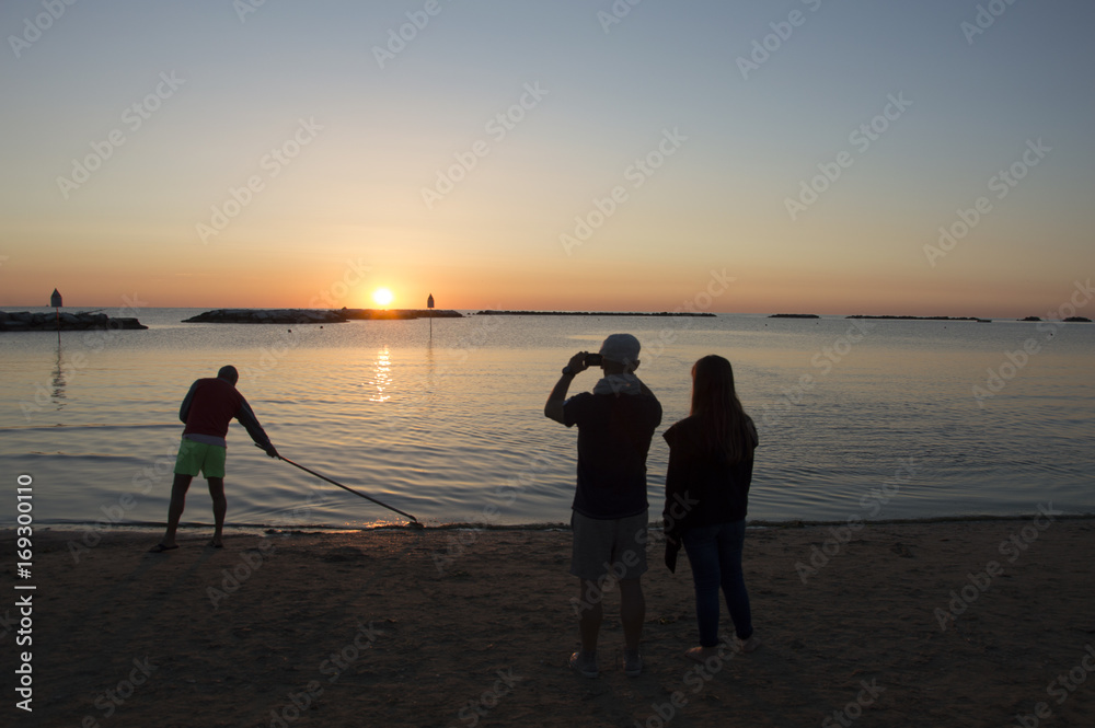 Couple make a photo to sunrise at sea while worker cleans the beach