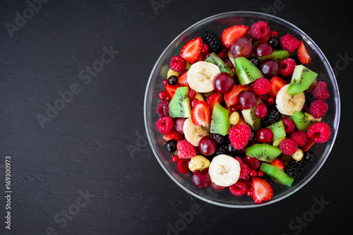 Natural breakfast, fruit salad in glass plate on black table. Flat lay, top view
