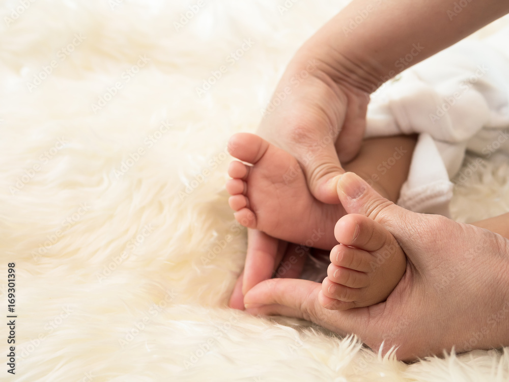 Mother holds her baby feet as a hand sign of heart on light creaam bed Mother holds her baby feet as a hand sign of heart on light creaam bed