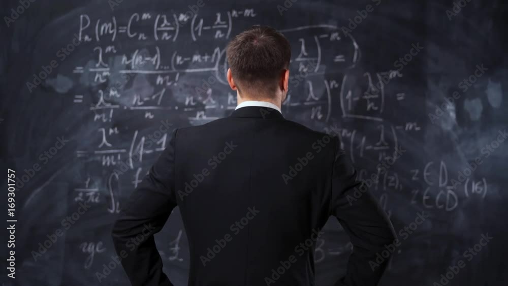 Rear view of man against chalkboard with math formula equations. He think about solution and try to understand high university task. Rear view of man against chalkboard with math formula equations. He think about solution and try to understand high university task.