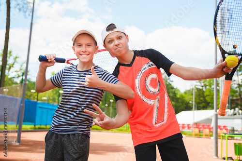 Cute boys playing tennis and posing in court outdoor