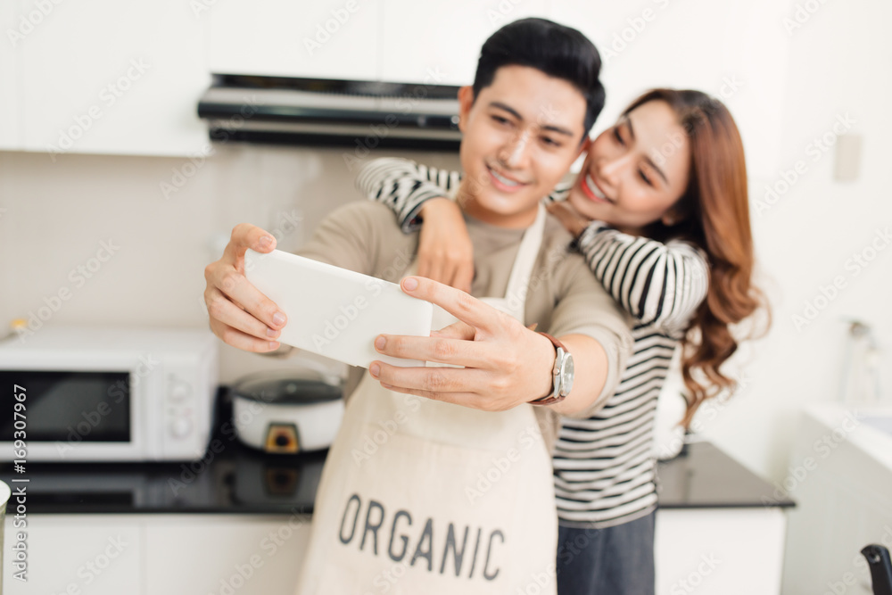 Happy asian couple smiling and cooking in the kitchen doing selfie using a smart phone Happy asian couple smiling and cooking in the kitchen doing selfie using a smart phone