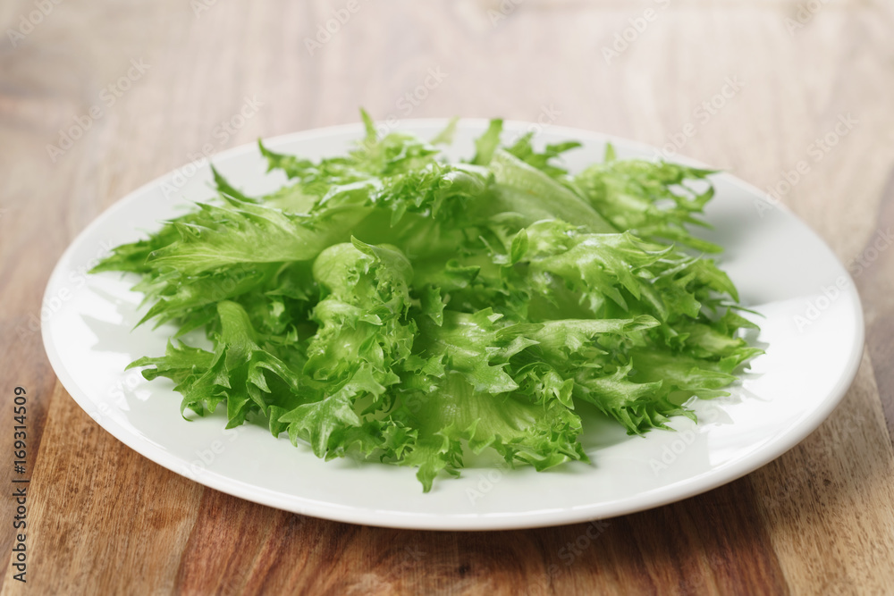 green frillice lettuce on white plate on wooden table green frillice lettuce on white plate on wooden table