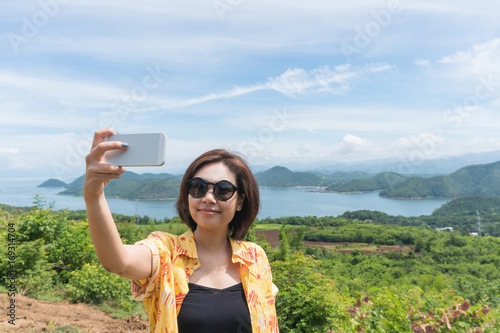 Female traveler selfie with her smart phone and beautiful landscape at kanchanaburi thailand