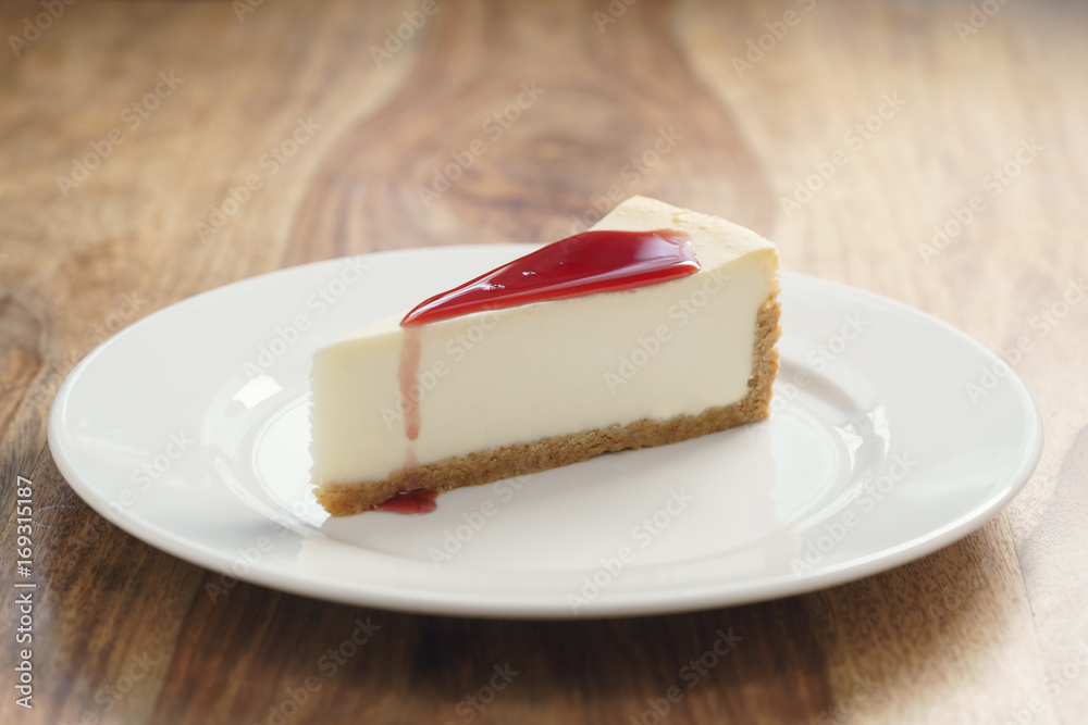 raditional new york cheesecake with berry jam on white plate on wood table