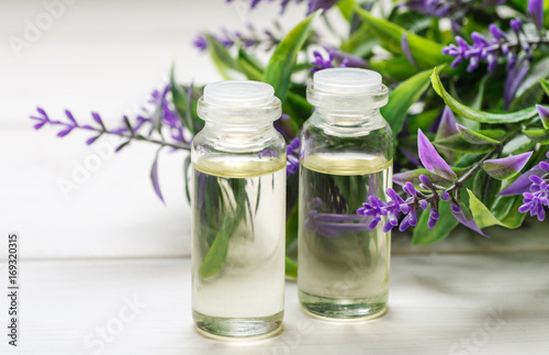 Two small glass bottles with liquid in it and lavender flower behind on a white wooden table