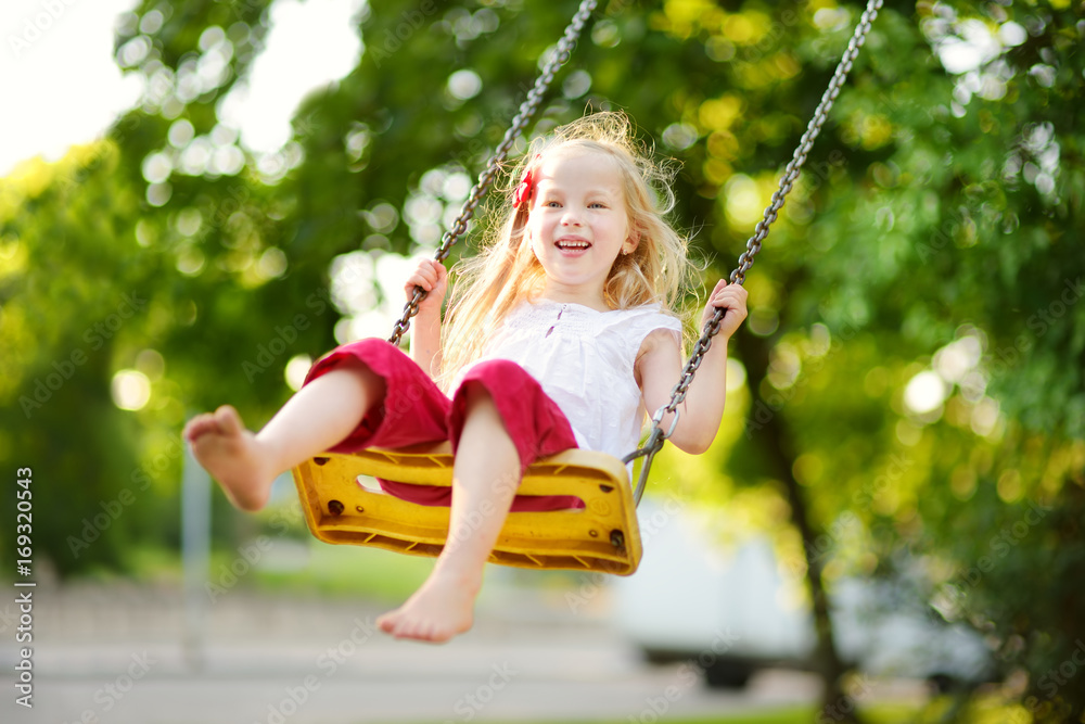 Cute little girl having fun on a playground outdoors on warm summer day