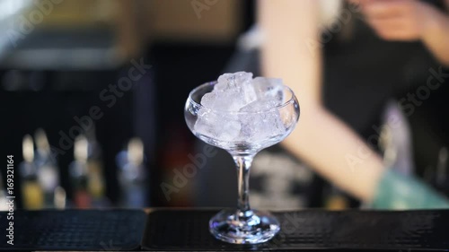 Close up of an unrecognizable woman bartender putting ice cubes into a cocktail glass and placing it on the counter. Handheld real time close up shot photo