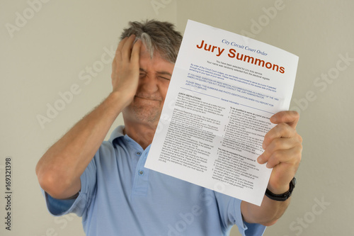 Angry upset man holding out his hand to show the jury duty summons he received in the mail which means he must be a juror on a court case.