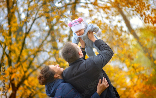 happy family walks in the autumn park, the father holds on hands and throws the kid