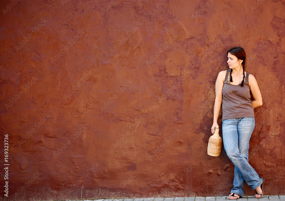 girl costs with a wine bottle near a wall of saturated color, waiting looks aside