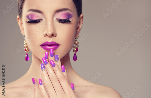 Beautiful girl model with fashion violet make-up and purple design manicure on nails . Jewelry and cosmetics , large violet earrings