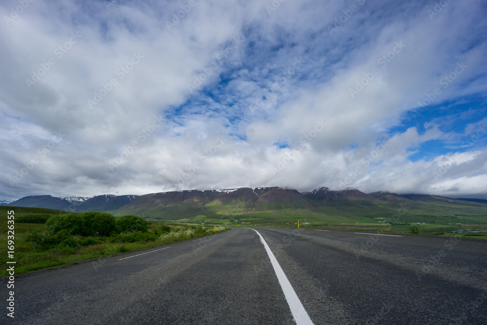 Iceland - Highway curve in front of majestic green mountain chain Iceland - Highway curve in front of majestic green mountain chain