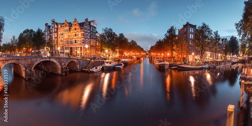Panorama of Amsterdam canal, bridge and typical houses, boats and bicycles during evening twilight blue hour, Holland, Netherlands. Used toning