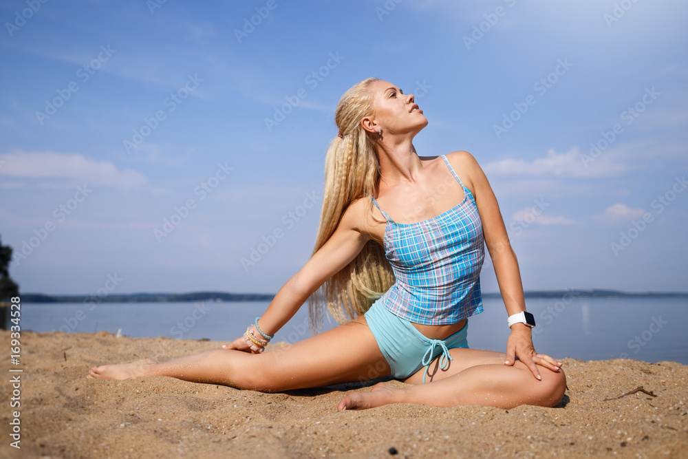 Blonde long haired girl in a blue suit is stretching and doing yoga on a lovely beach in sunlight of the rising sun Blonde long haired girl in a blue suit is stretching and doing yoga on a lovely beach in sunlight of the rising sun