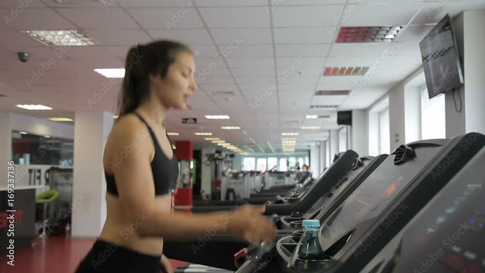 Young woman running on treadmill in sports club indoors. atlete walks and then jogging on mill in spacious premise with professional fitness equipment.