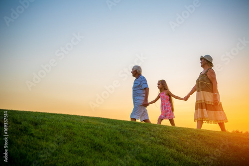 Girl with grandparents at sunset. People on sky background. photo
