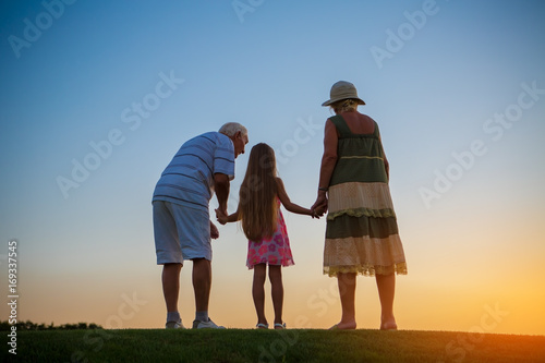 Girl and her grandparents. People standing on sunset background. Admiring the infinity.