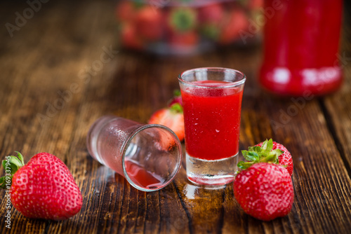 Portion of Strawberry liqueur on wooden background, selective focus