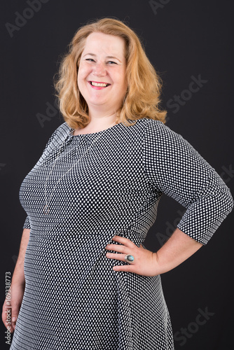 Portrait of a attractive european light overweighted red haired female in white black dress smiling friendly in front of black backgrouind - half body studio shot