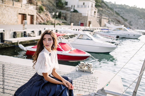 Beautiful girl walking on the pier by the sea near the yacht, boats in the blue long dress © boykovi1991