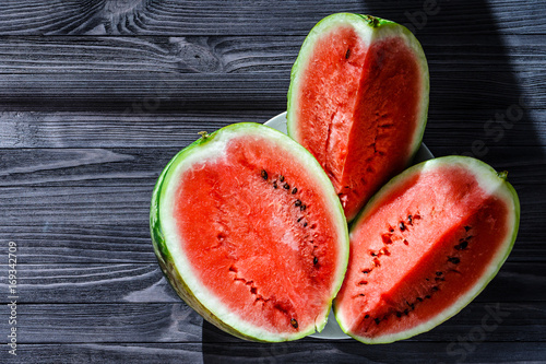 Background of three slices of a cut watermelon in a white plate on a black wooden table top view. Empty space for text