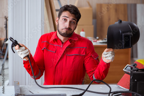 Young repairman with a welding gun electrode and a helmet weldin photo