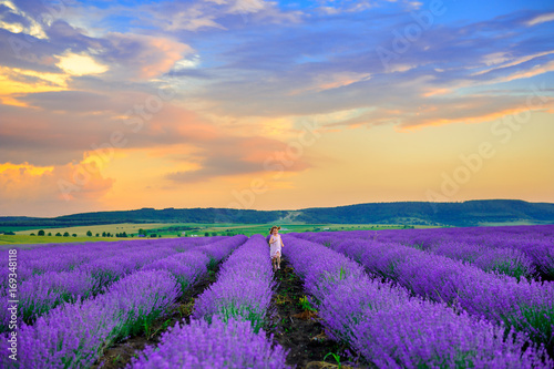 Happy girl in platitse rejoices and runs in the lavender field at sunset