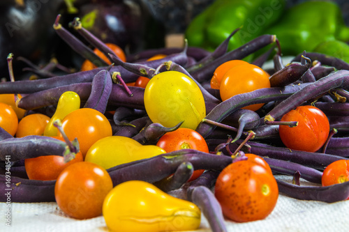 Horizontal photo of colorful tomatoes, purple beans, bell peppers, and eggplant on a white surface photo