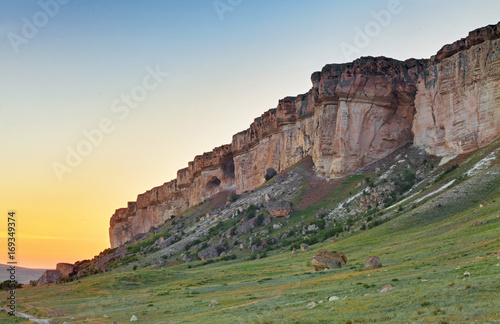 Vertical rocky wall at sunset with large boulders at the foot